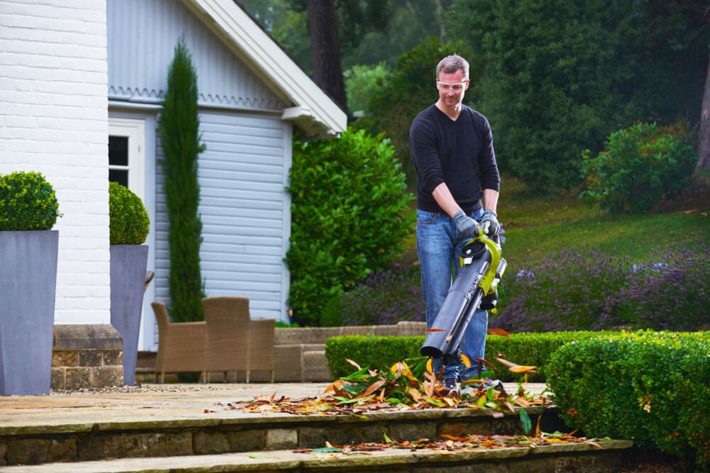 Mężczyzna używa dmuchawy do sprzątnięcia liści na schodach tarasu przed domem
