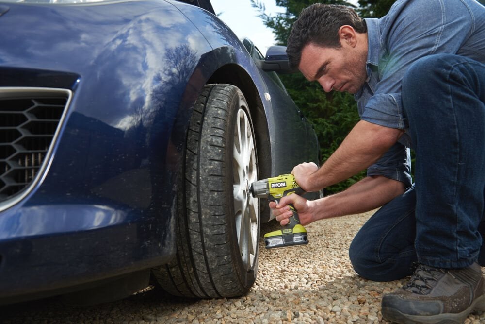 Mężczyzna używa wkrętarki do kół samochodowych