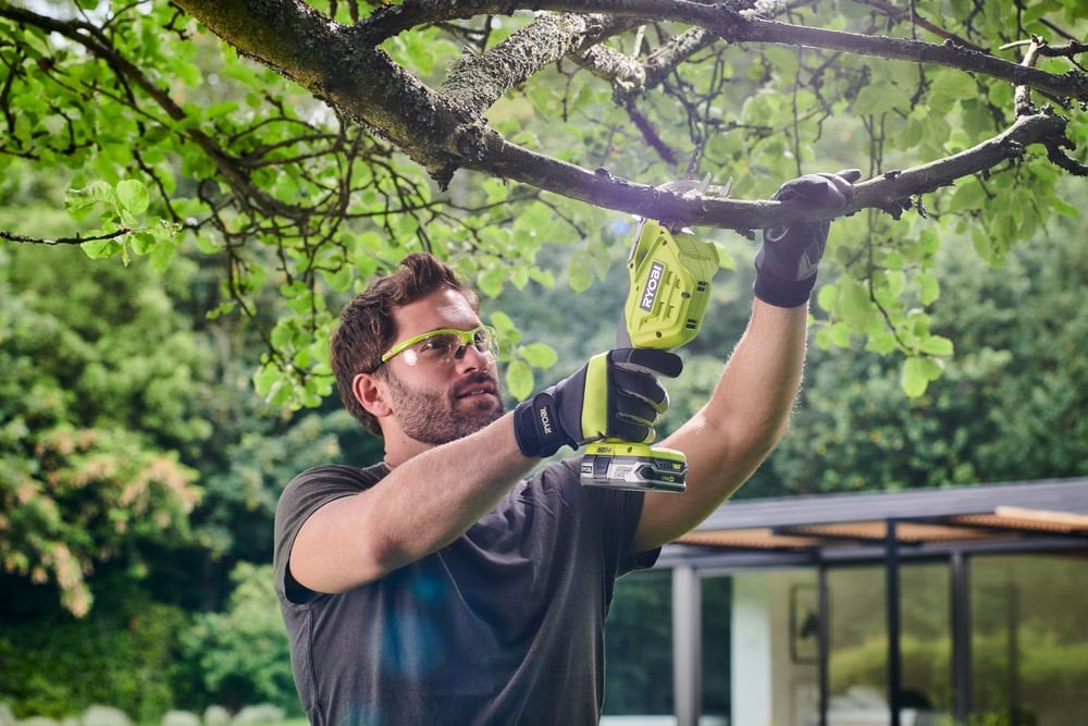 Mężczyzna używa miniaturowej pilarki szablastej 18V ONE+ do cięcia gałęzi
