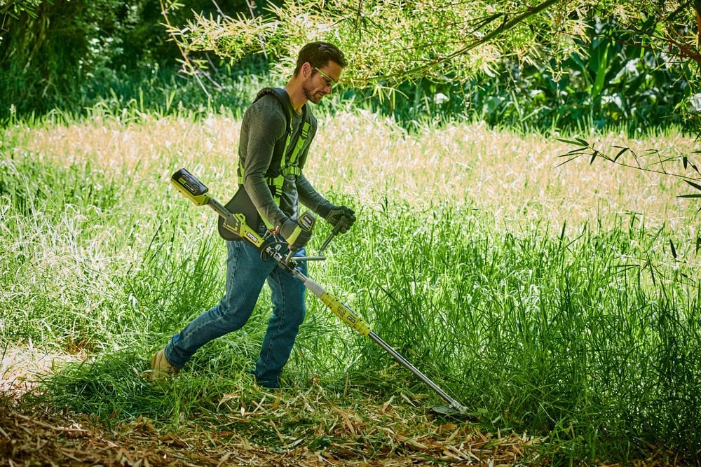 Mężczyzna tnie wysoką twardą trawę kosą akumulatorową RYOBI