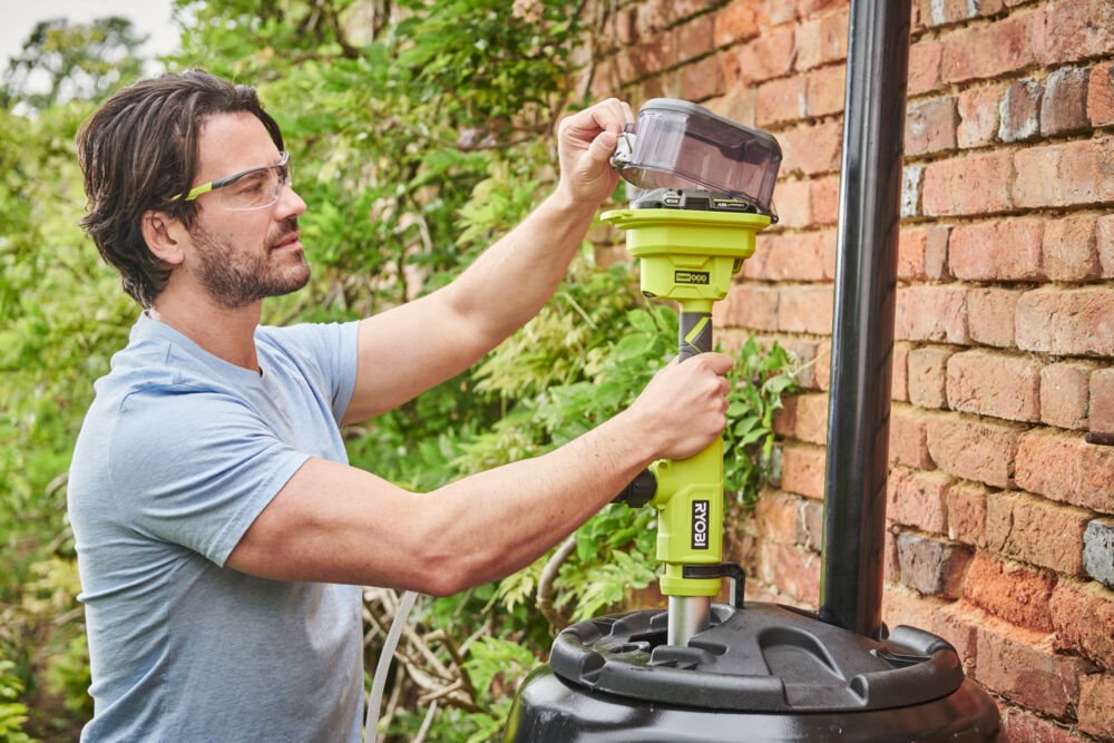 Mężczyzna montuje teleskopową pompę wodną w beczce deszczówki