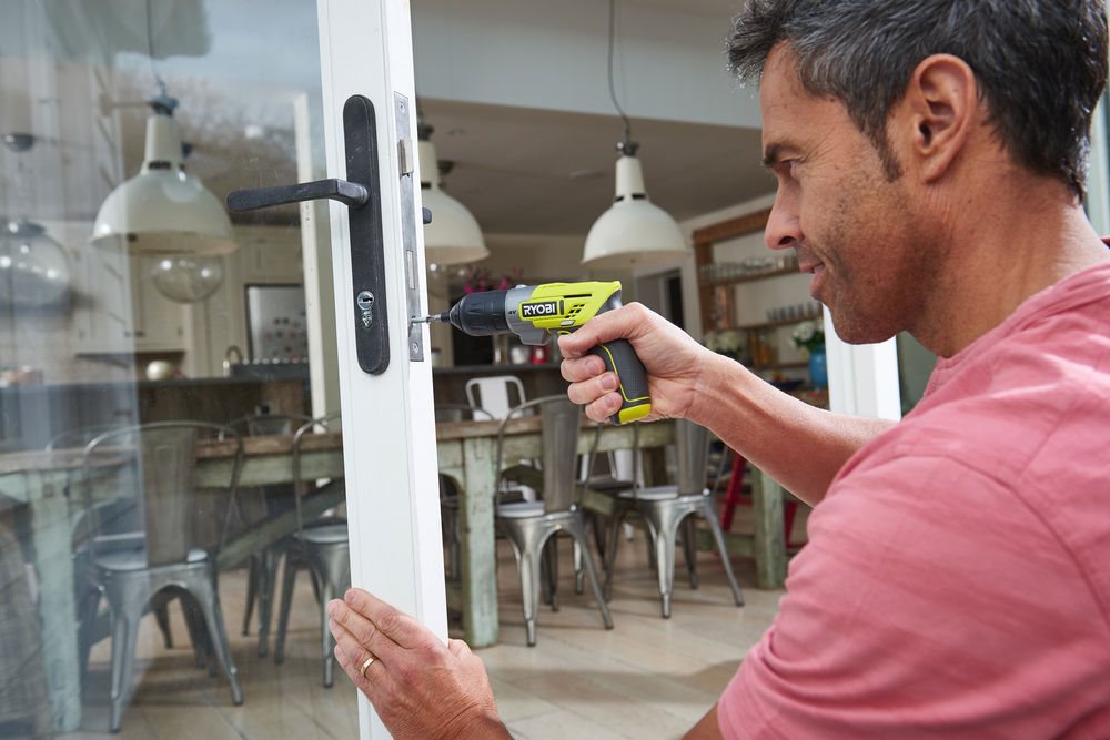 Mężczyzna używa małej wkrętarki do naprawy klamki w drzwiach balkonowych