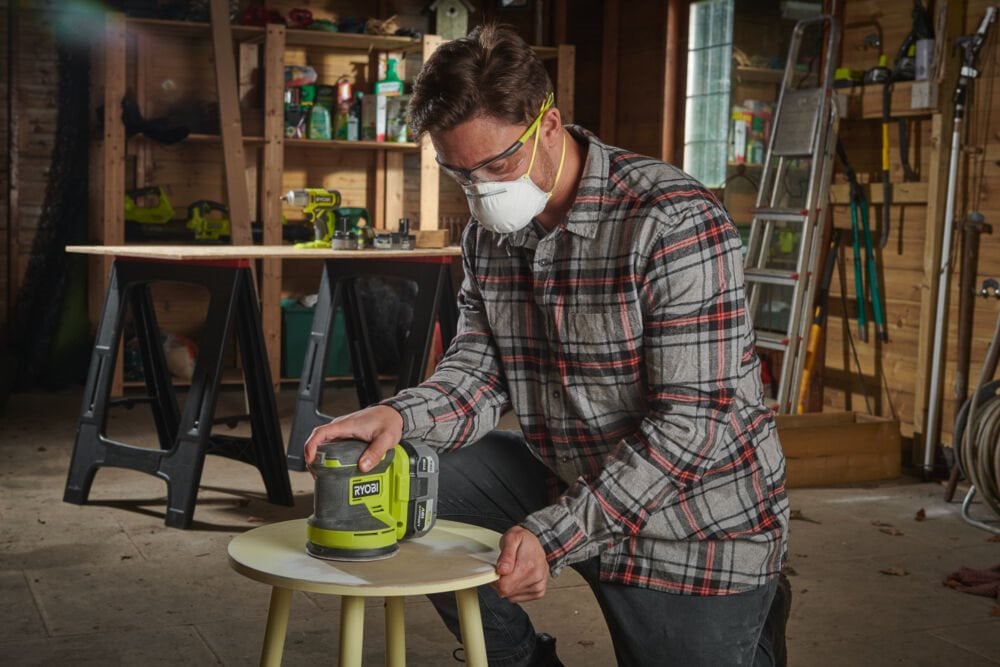 Mężczyzna w warsztacie używa szlifierki mimośrodowa 18V RYOBI